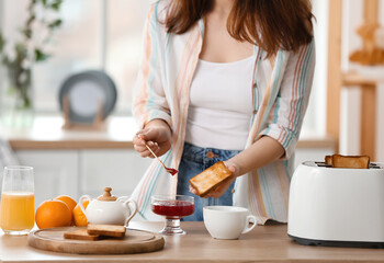 Beautiful young woman making tasty toasts in kitchen