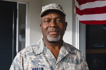 Portrait of serious african american senior man soldier in camouflage clothing and cap against house