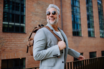 Confident man wearing backpack walking in street, businessman in casual clothes in summer on the way to work.