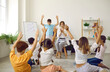 © Studio Romantic - Students and teacher having fun in class. Kids playing charades or Simon Says game at school. Small group of children sitting on floor in classroom, looking at classmate and repeating his movements