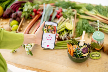Holding smart phone with running mobile application for track calories consumed on background of healthy food ingredients. Concept of modern technology in proper nutrition