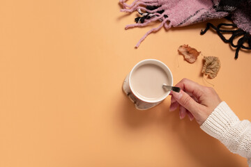 Female hand in sweater holding cup of cocoa on colored background, top view with copy space