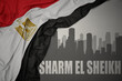 canvas print picture - abstract silhouette of the city with text Sharm El Sheikh near waving colorful national flag of egypt on a gray background.