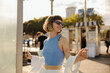 © Look! - Beautiful young caucasian girl with brown hair with tattoo walks in summer city center. Model wears sunglasses, blue tank top and white shirt. People sincere emotions lifestyle concept.