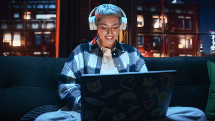 Fototapete - Young Beautiful Woman Wearing Headphones and Working from Home on Laptop Computer in Cozy Stylish Loft Apartment. Creative Female Smiling, Checking Social Media, Browsing Internet.