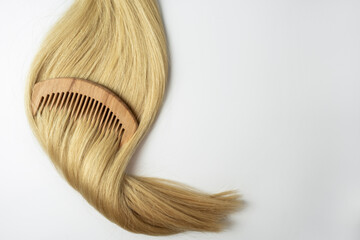 Wall Mural - A strand of blonde hair with a wooden comb on it lying on a white background