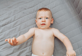 a small child is lying alone on a wide bed. the kid is looking at the camera with his legs tucked under him. top view