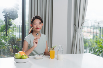 Wall Mural - Portrait of beautiful young woman having breakfast in the kitchen.