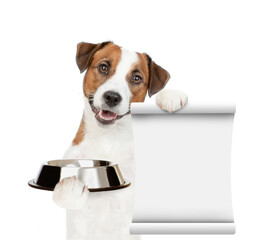 Poster - Hungry jack russell terrier puppy holds empty bowl and shows empty list. isolated on white background