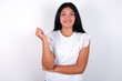 © Jihan - Cheerful young brunette woman wearing white T-shirt standing against white background with hand near face. Looking with glad expression at the camera after listening to good news. Confidence.