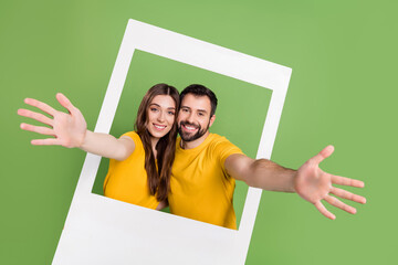 Wall Mural - Portrait of positive handsome guy pretty lady raise hands invite through album card isolated on green color background