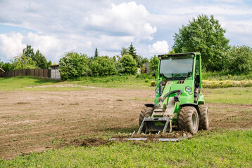 Wall Mural - A green mini skid steer loader clear the construction site. Land work by the territory improvement. Small tractor with a ground leveler for moving soil, turf. Machine for agriculture work. Copy space