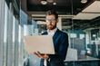 © Prostock-studio - Business person. Successful middle aged businessman with laptop in hands standing in modern office interior