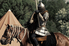 Knight In Armor On A Horse With A Spear. Defender On Guard. Brown Warhorse With Rider.