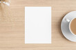 White invitation card mockup with a dry flower on the wooden table. 5x7 ratio, similar to A6, A5.