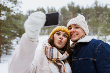 Poster - season, technology and leisure concept - happy couple with smartphone taking selfie in winter park