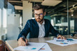 © Prostock-studio - Concentrated handsome businessman in glasses working with documents in office interior, checking and signing papers