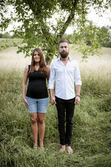 Wall Mural - pretty young pregnant woman with black shirt is standing with her boyfriend in a high meadow and they are happy and full of anticipation for the baby