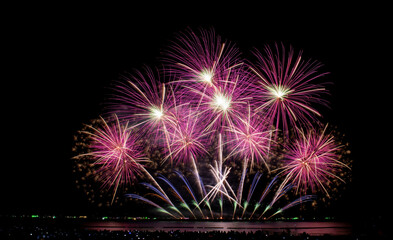 Colorful magical fireworks showing on sea in celebration festival with city lighting and black sky background. 