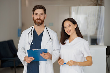 Wall Mural - Portrait of happy doctor and nurse standing near reception in hospital and looking camera