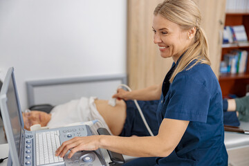 Wall Mural - Smiling doctor ultrasound examine senior patient abdomen at hospital. Prenatal diagnosis center