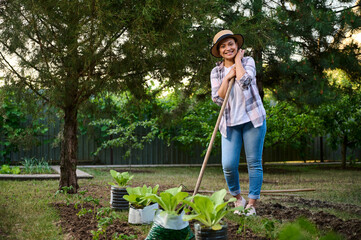 Charming African American woman, gardener smiles at the camera, posing with a hoe while working in the vegetable garden