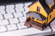 Miniature yellow house sitting on a white computer keyboard real estate vacation rental home