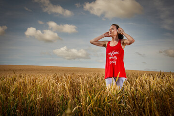 woman standing in a field listening to music on headphones, positive vibes only t shirt.