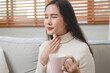 © Pormezz - Sore throat in flu season. Young asian woman touching her neck and feeling pain in throat in the bedroom at home.