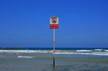 Multilingual Warning Sign, On The Beach In Front Of An Empty Sea. A Plate With An Inscription In Different Languages ​​about The Prohibition Of Swimming In The Sea. 