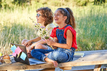 Full Body Of Laughing Boy And Girl With Bouquet Of Wildflowers Having Fun While Browsing Laptop Together During Picnic In Nature