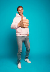 Sticker - Full size photo of cheerful man smiling and showing thumbs up at camera isolated over light blue background.