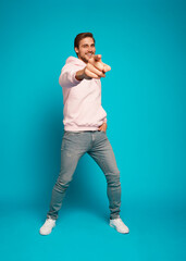 Sticker - Full size photo of smiling brunette man pointing finger at camera isolated on light blue background.