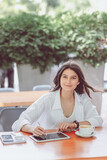 Fototapeta  - Caucasian lovely young enthusiast blogger girl sitting with digital tablet for designer and cup of coffee during language class in cafe on terrace outside. Remote and freelance successful job concept