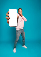 Wall Mural - handsome excited man showing pointing at empty smartphone screen posing over light blue background, 