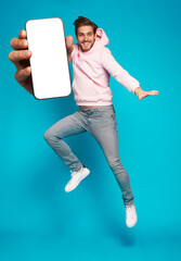 Wall Mural - handsome excited man showing pointing at empty smartphone screen posing over light blue background, 