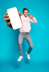 Wall Mural - handsome excited man showing pointing at empty smartphone screen posing over light blue background, 