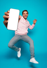 Wall Mural - handsome excited man showing pointing at empty smartphone screen posing over light blue background, 