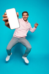Wall Mural - handsome excited man showing pointing at empty smartphone screen posing over light blue background, 