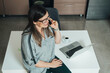 © Tijana - High angle view of happy business woman talking on her smartphone while leaning on a kitchen desk with a laptop computer and cup of coffee