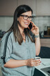 © Tijana - Smiling Businesswoman Drinking Coffee And Talking On A Mobile Phone At Home