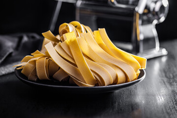 Wall Mural - Uncooked pappardelle pasta on plate on black table.