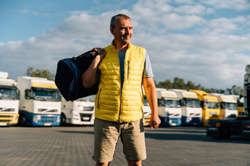 Wall Mural - Portrait of caucasian mature man with bag on some-truck vehicles parking background. Truck driver worker 