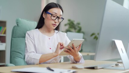 young beautiful asian woman general practitioner sitting female doctor working using digital tablet front of computer at the workplace. healthcare medical tech app in software web program at hospital