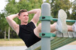 © Евгений Шемякин - Happy fit fitness handsome athletic guy, young man training abs on bench, doing abdominal exercise on a public equipment in outdoor fitness park. Workout and bodybuilding concept, healthy lifestyle.