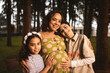 © Pablo - pregnant latin mom hugging her son and daughter in pine forest looking at the camera
