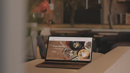 Wall Mural - No people shot of food delivery website on laptop screen on wooden table in modern restaurant or cafe