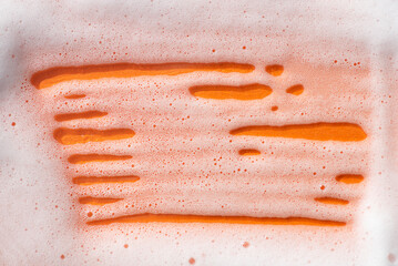 Wall Mural - Foam on an orange background. Soapy liquid texture with bubbles. Natural sunshine and shadows. Skincare cleansing cosmetic