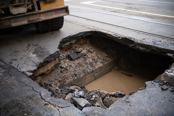 Wall Mural - Huge sinkhole on busy asphalt road surface on which cars drive. Accident situation on a city street due to cracks in asphalt. Broken hole filled with muddy water.