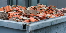 Red Bricks Debris In Construction Metal Waste Container Close Up. Building Demolition And Remove.